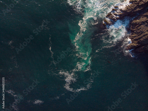 Aerial photograph. Seething dark turquoise ocean water and a piece of rocky shore. Beautiful seascape. Bright colours. Sea travel, trade, tourism, ecology.