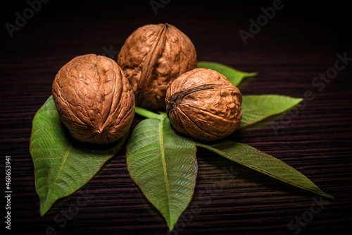 Whole walnuts with green leaves, on wooden background
