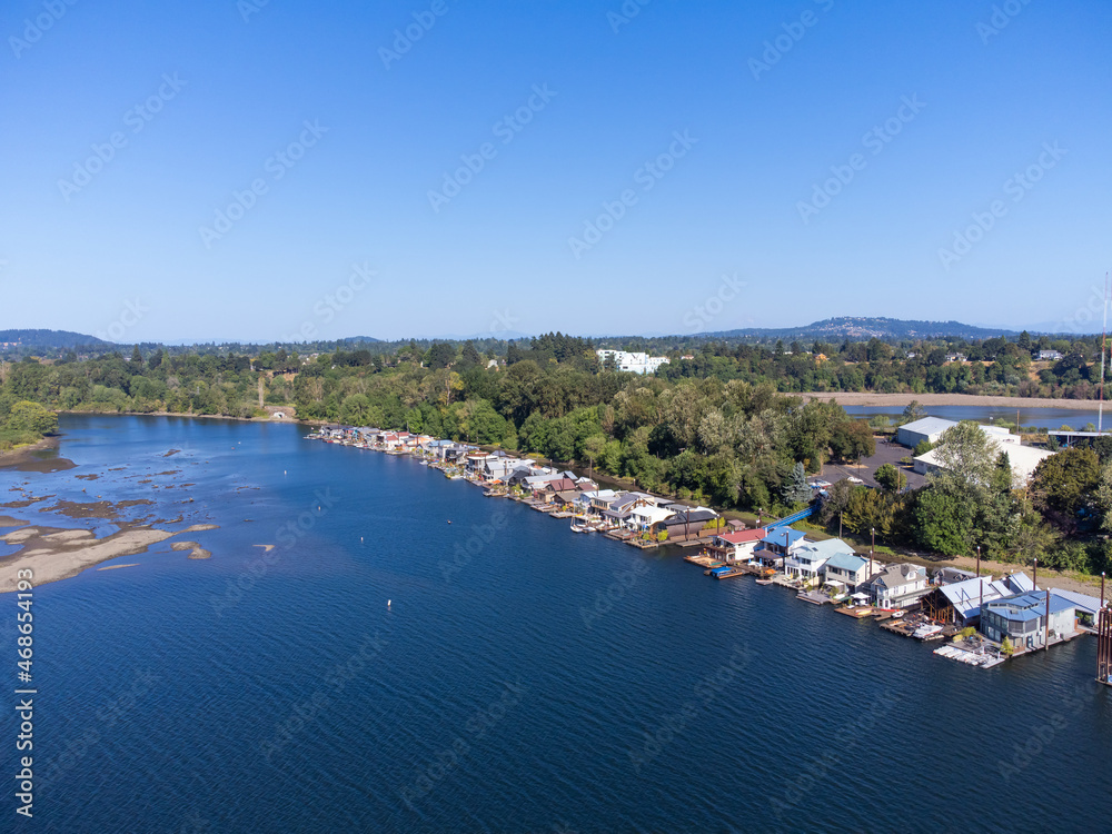 A big blue river, on which boats are moored, and a small green town on the shore. Cloudless blue sky. Beautiful nature, calm scenes. Postcard, housing, tourism, recreation.