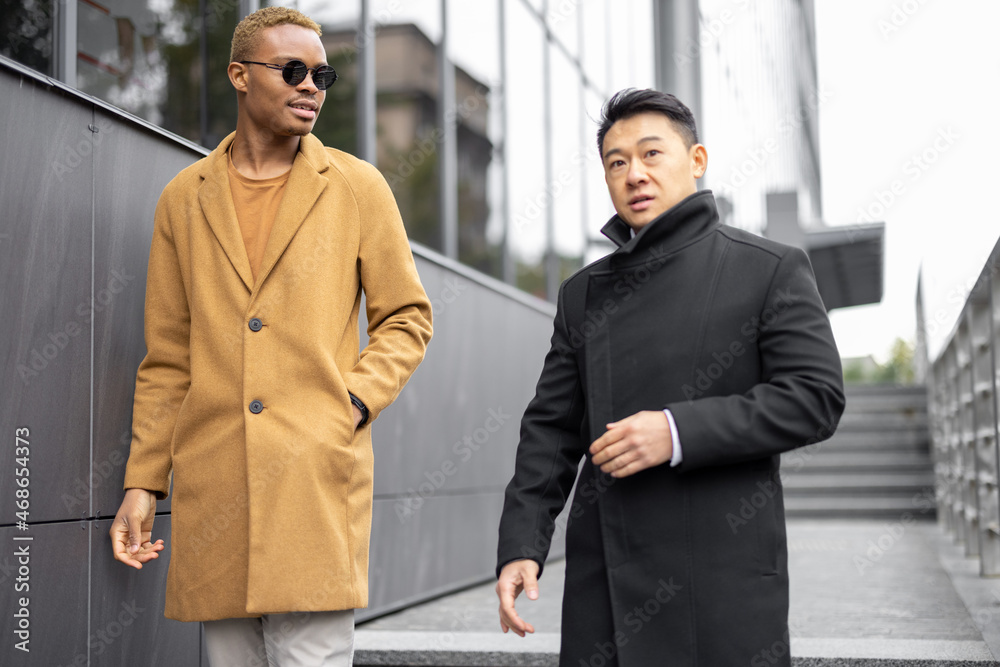 Businessmen walking on city street and talking. Concept of remote and freelance work. Idea of business cooperation. Successful entrepreneurs. Young guy in glasses. Autumn season Businessmen walking on city street and talking. Concept of remote and freelance work. Idea of business cooperation. Successful entrepreneurs. Young guy in glasses. Autumn season