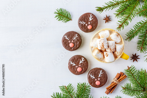 Christmas coffee with marshmallows and chocolate biscuits with deer faces on white background decorated with fir twigs.