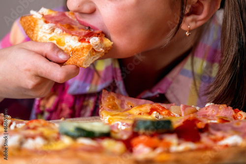 Young beautiful attractive girl enjoys delicious slice of  pepperoni pizza. Horizontal image.