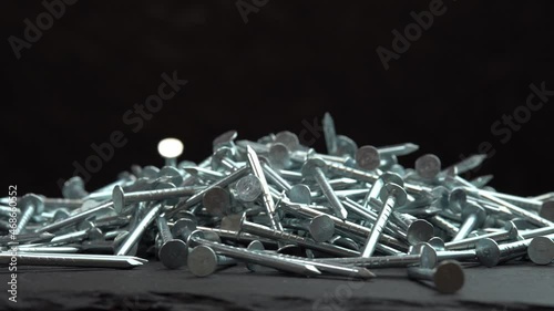 Metal steel nails for construction work falling on a rotating surface on a black background, hobnails are spinning close up background, pin or spike for construction work photo