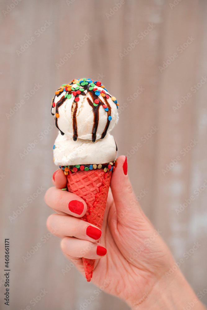 Close-up of woman's hand holding vanilla ice cream cone. Vanilla ice cream cone with sugar sprinkles and chocolate in woman hand on light background Close-up of woman's hand holding vanilla ice cream cone. Vanilla ice cream cone with sugar sprinkles and chocolate in woman hand on light background