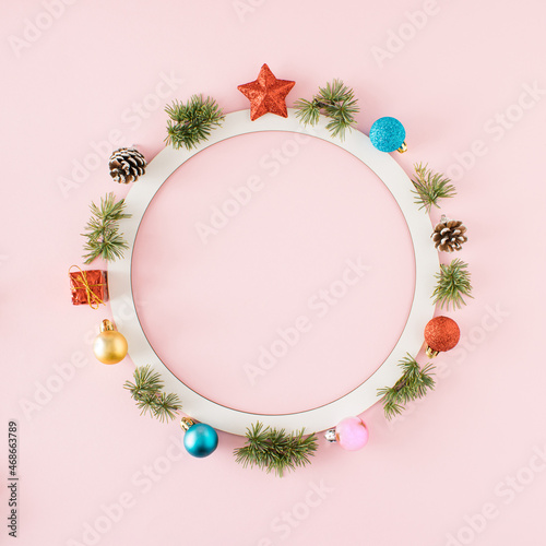 Christmas decorations and Christmas tree twigs arranged around a round white frame on a pink background. There is copy space in the middle