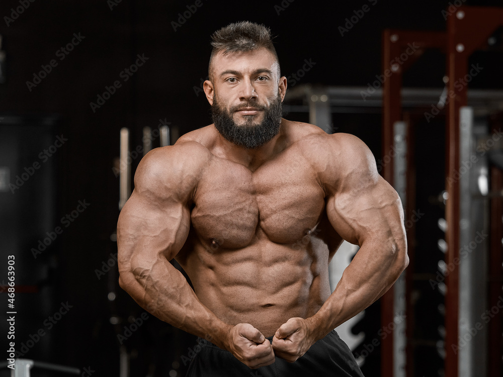 Brutal muscular bodybuilder in perfect athletic form posing in the gym. Sport and healthy lifestyle concept Brutal muscular bodybuilder in perfect athletic form posing in the gym. Sport and healthy lifestyle concept