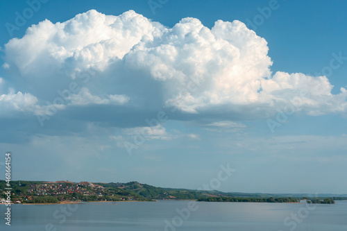 group of white cumulus clouds on blue sky over hilly river bank as natural background © westermak15