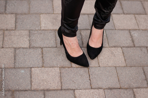women's legs in leather pants and black heeled shoes on the background of street tiles