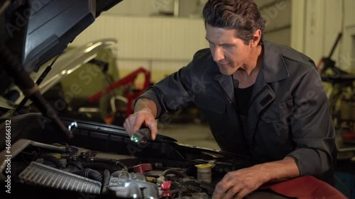 We have a problem. Auto mechanic standing at the opened hood and lighting with lamp while working at the workshop and air filters. Maintenance concept