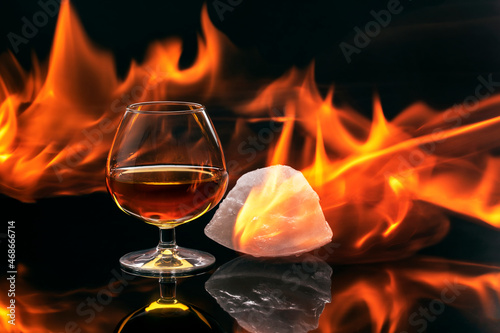 Brandy glass with a piece of ice surrounded by flames, concept