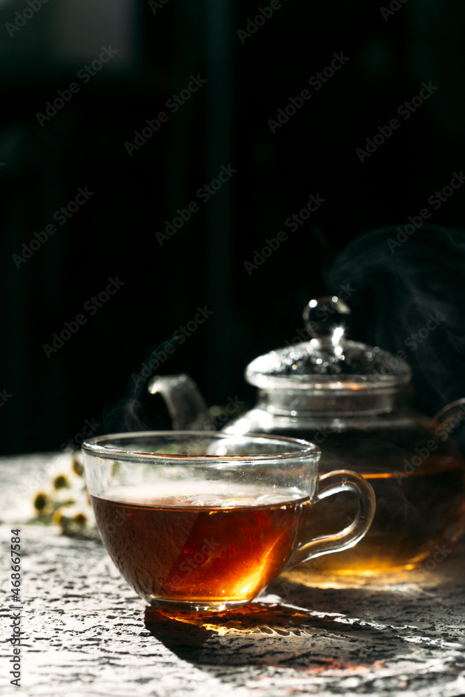 Warm cup of tea with glass teapot on dark background Warm cup of tea with glass teapot on dark background