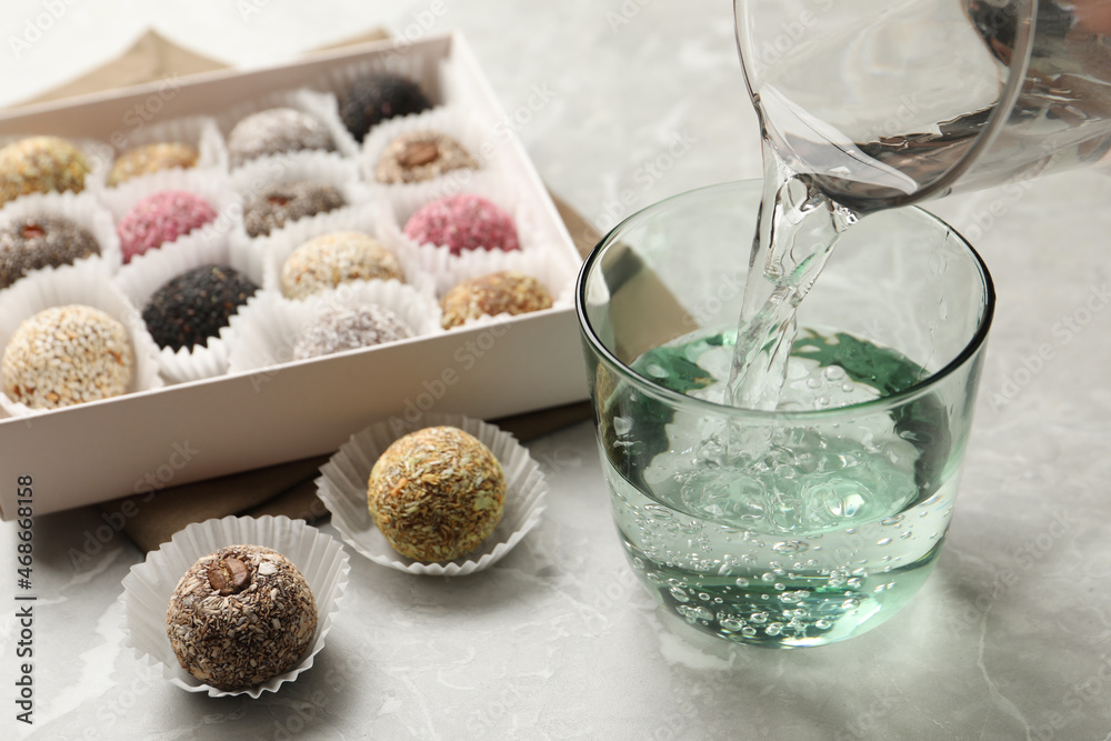 Pouring water into glass and delicious vegan candy balls at light grey marble table
