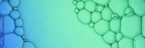The surface of the bubbles. Extreme close-up of soap foam structure on green and blue. Cosmetic background with copy space. Banner format