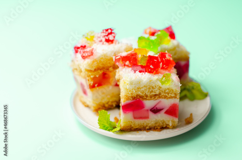 A portion of cream cake with pieces of colourful jelly and sprinkled with coconut flakes