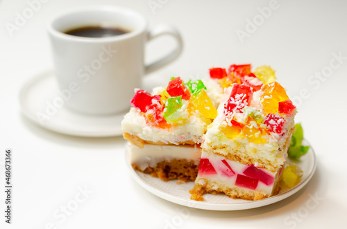 A portion of cream cake with pieces of colourful jelly and sprinkled with coconut flakes