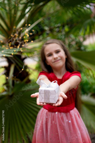 Little girl on a background of palm trees holds a gift in her hands.