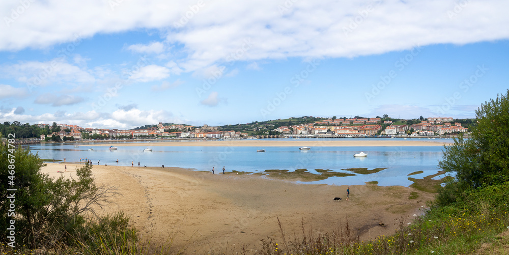 Paisaje panorámico de San Vicente de la Barquera con barcas en el agua, y arena en la playa  en Cantabria, España, en el verano de 2020.
