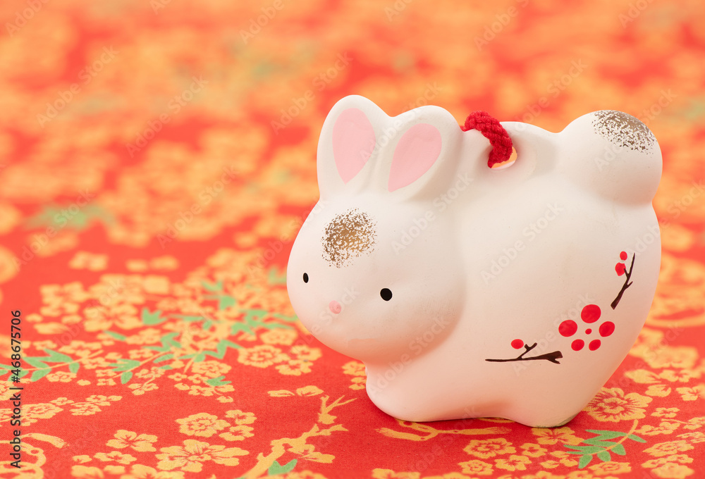 Old ceramic rabbit on red patterned fabric background.