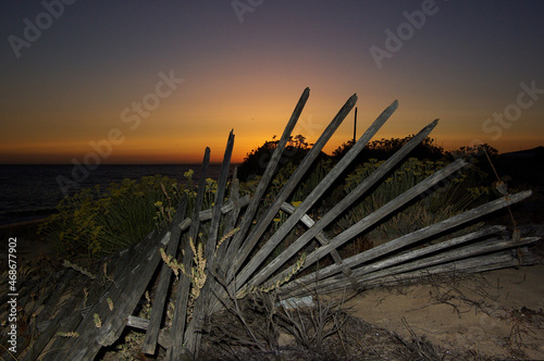 A broken wooden fence on a beach at sunset, lit by flashlight