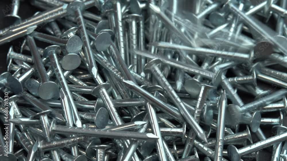 Metal steel nails for construction work falling on a rotating surface, hobnails are spinning close up background, pin or spike for construction work Metal steel nails for construction work falling on a rotating surface, hobnails are spinning close up background, pin or spike for construction work