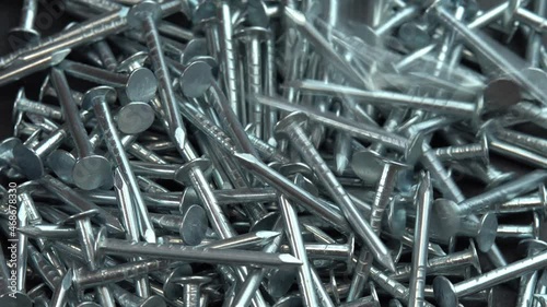 Metal steel nails for construction work falling on a rotating surface, hobnails are spinning close up background, pin or spike for construction work photo