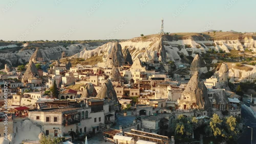 Drone flying close above beautiful small sunny ancient town among big historic white rocks in summer Cappadocia Turkey.