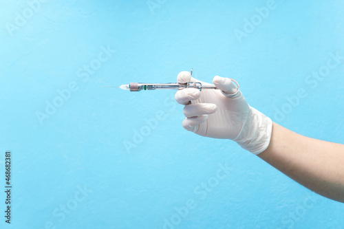 Dental anesthesia syringe, young woman's hand with a white latex glove, nitrile glove, holding a syringe, on a blue background.
