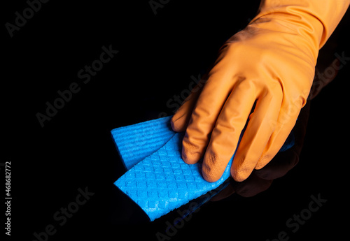 A gloved hand cleans a black table with a blue napkin. Close-up shot of home cleaning process. Healthcare during coronavirus and disinfection concept