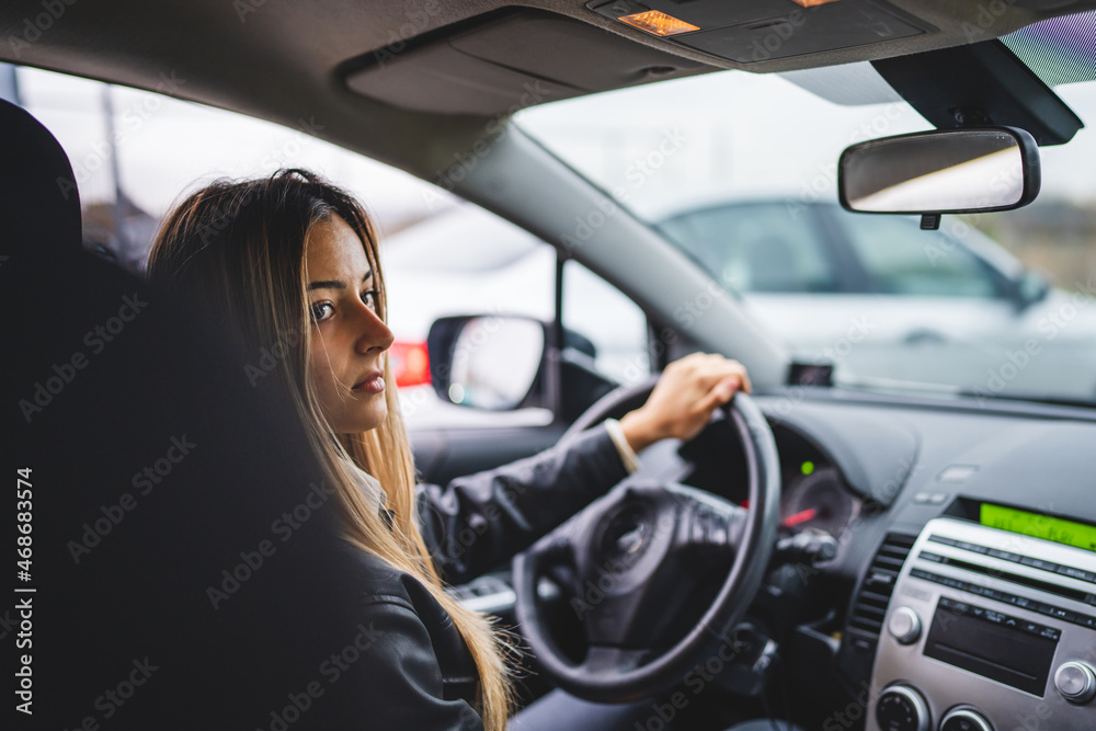 Young adult one caucasian woman driving car waiting while holding wheel looking to the side back view female driver copy space real people