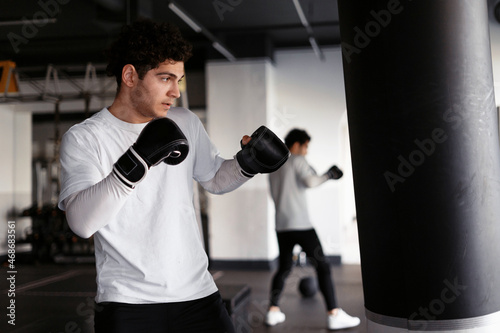 Man sports in the boxing club. An athlete does an exercise on equipment with a pear. The coach trains actively. Blows with gloves.