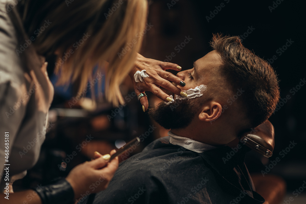 Man getting shaved with straight edge razor by hairdresser at barbershop