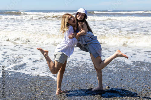 Two young women play together outside at the beach with the Pacific ocean behind them
