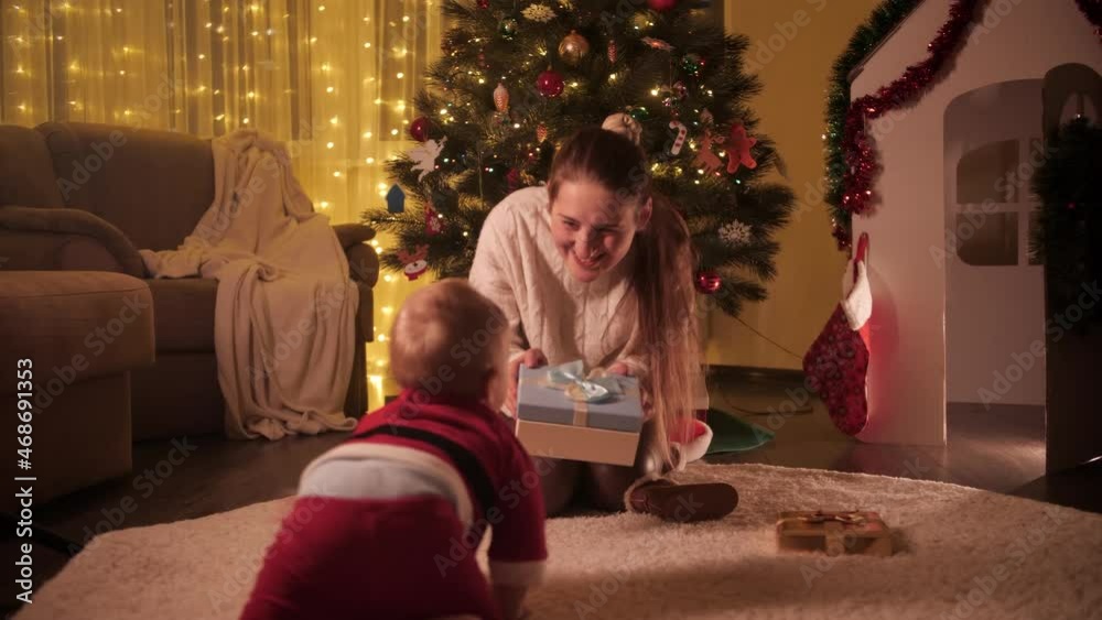 Little baby boy in Santa Claus costume crawling to his mother sitting under Christmas tree. Families and children celebrating winter holidays. Little baby boy in Santa Claus costume crawling to his mother sitting under Christmas tree. Families and children celebrating winter holidays.