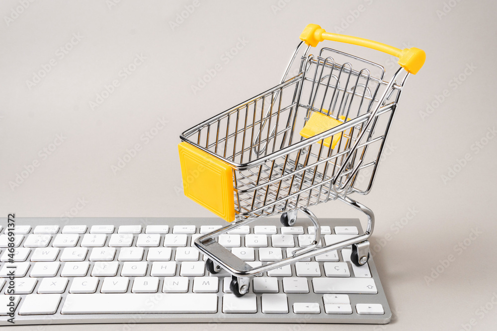 miniature shopping cart on a computer keyboard on gray background with copy space