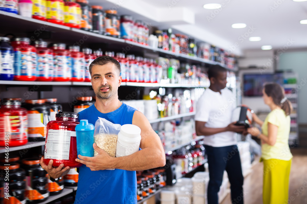 Muscular man with jars of sports nutritional supplements in store
