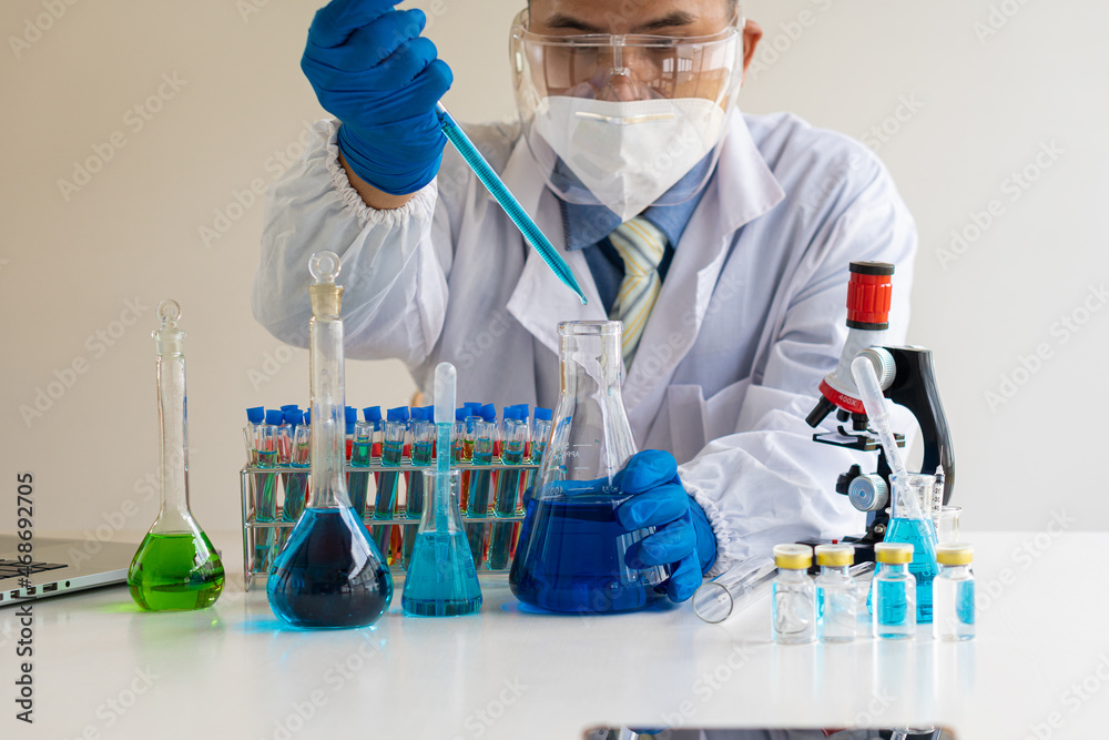 Fototapeta premium A biochemical research scientist working to develop a vaccine against coronavirus in a drug research laboratory holding a vial with glassware. Research and development concepts in science laboratories