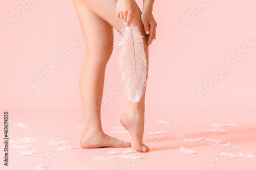 Legs of young woman with soft feather on color background. Epilation concept