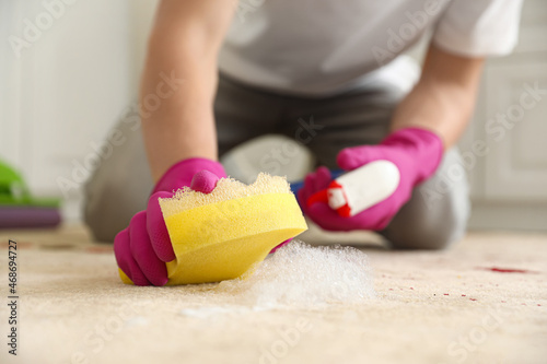 Young man cleaning carpet with sponge in kitchen, closeup