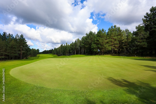 Golf course, landscape, green grass on the background of the forest and a bright sky with clouds. High quality photo