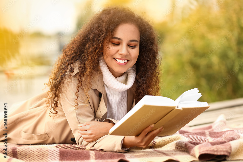 Obraz premium Happy African-American woman reading book on sunny autumn day