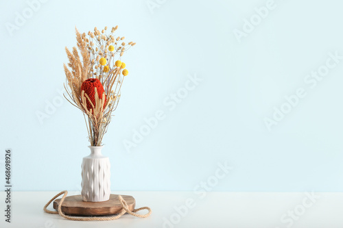 Vase with beautiful dried flowers on table near blue wall