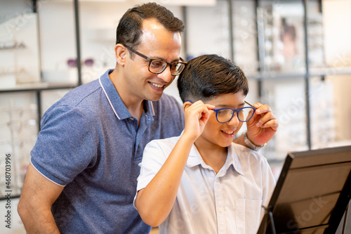 Fotografía Indian father hold glasses that his son wear and look to mirror with happiness during come to optical shop for buying new glasses