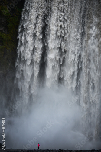 The stunning and popular Skogafoss waterfall cascades behind a tourist, Skogar, South Coast of Iceland photo
