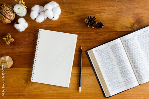 Open Bible with notebook and cotton flowers on a wooden table.