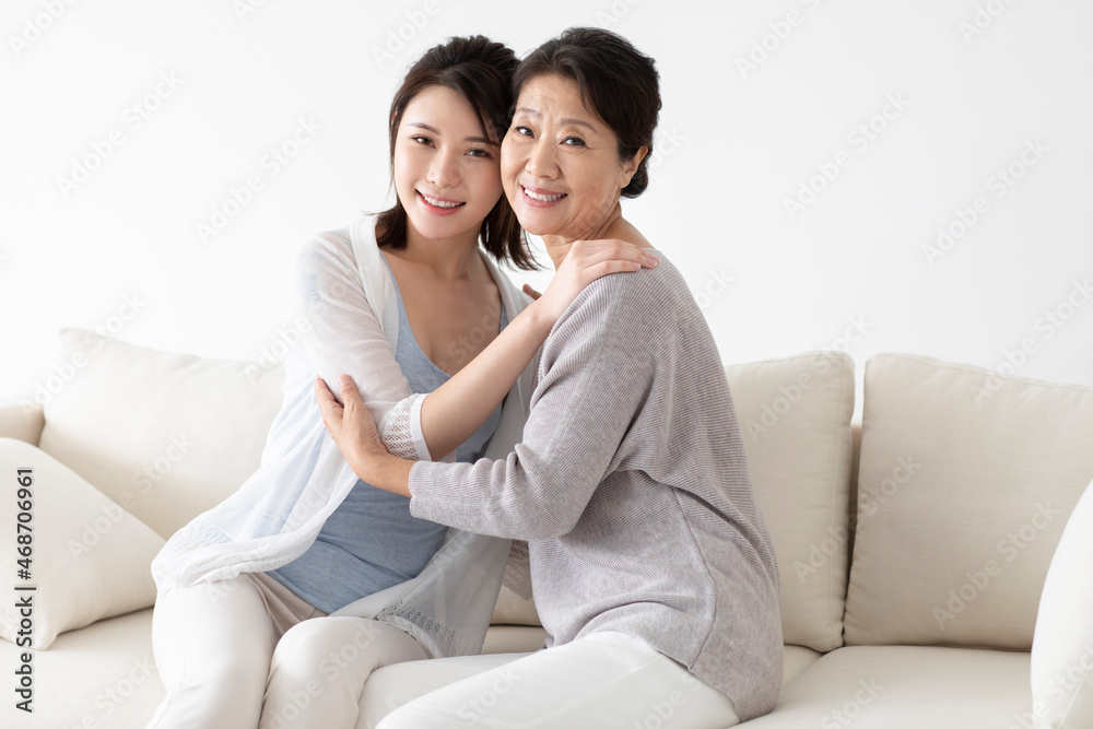 Cheerful Chinese mother and daughter sitting on sofa Cheerful Chinese mother and daughter sitting on sofa