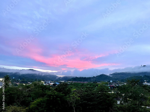 Beautiful pink sunset over the valley. Bright glow of the sun. Top view of the town in summer. Peaks of the mountains are fog of clouds. Panorama. Amazing landscape. Evening in the countryside.
