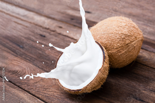 Brown coconut with coconut milk splash isolated on wooden table background. photo