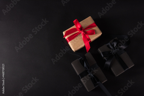 Black Friday Sale shopping concept, Top view of gift box wrapped black paper and black bow ribbon present around the brown box with red bow ribbon, studio shot on dark background
