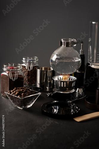 Vacuum coffee maker also known as vac pot  siphon or syphon coffee maker and toasted coffee beans on rustic black stone table. Copy space for your text