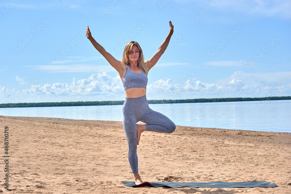 A woman does yoga on a sandy beach against the background of a river A woman does yoga on a sandy beach against the background of a river